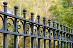 a close up of a wrought iron fence with trees in the background